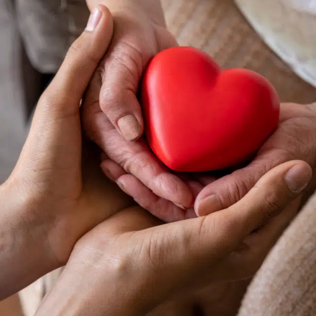 Heart Health Tips for Older Adults Feature Image: Taking care for the elderly concept with a wrinkled hands and young hands holding a red heart shape