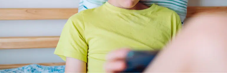 School age boy playing video game using mobile at home lying down on bed