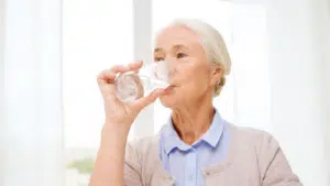 Tips for Water Intake for Older Adults Feature Image: Happy senior woman with glass of water at home